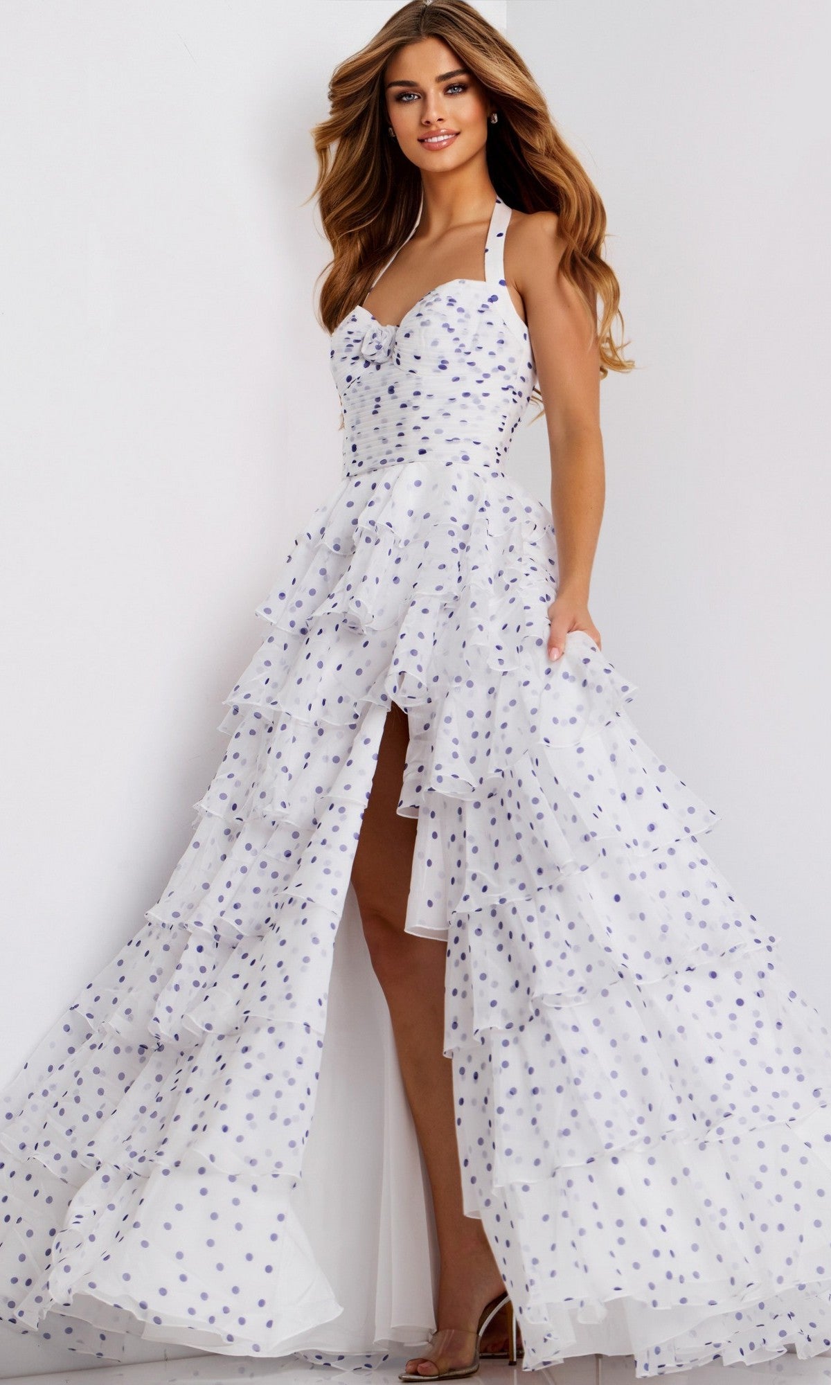 A woman poses against a plain white background wearing the Jovani 49776 long prom dress, featuring white polka dots, ruffles, a sweetheart halter neckline, thigh-high slit, and fitted bodice.